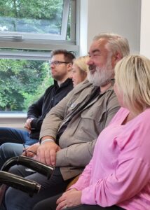 Four people sat in a row, one person is talking about the others are turning to listen.