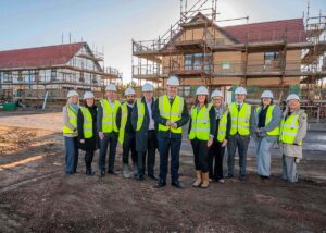 A group of eleven people wearing hart hats and yellow high viz jackets standing on a construction site for new homes.